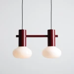 Lampa wisząca Flo Ruby z dwoma kloszami w kolorze mlecznym, zawieszona na czarnym przewodzie. Konstrukcja z metalowych elementów w kolorze czerwonym, z prostym, nowoczesnym designem.