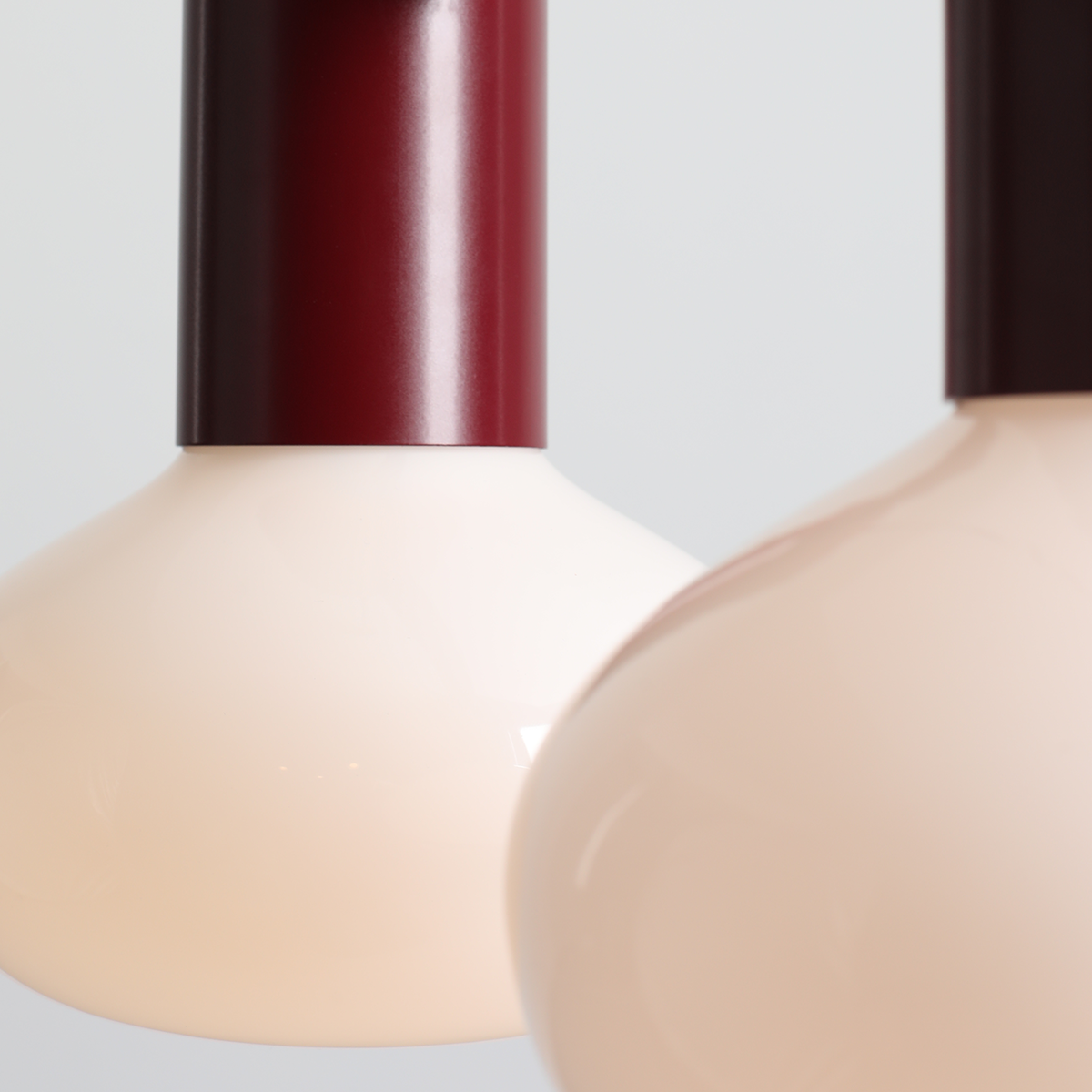 Lampa wisząca Flo Ruby z dwoma kloszami w kolorze jasnego różu, zawieszona na czerwonym metalowym mocowaniu. Klosze mają zaokrąglony kształt, tworząc nowoczesny design. Produkt umieszczony na jednolitym tle.