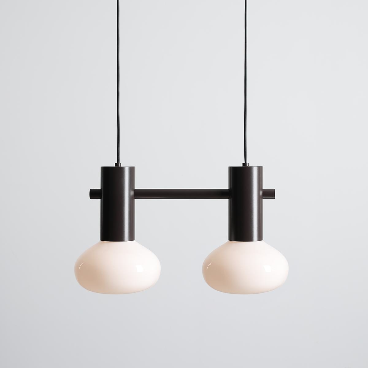 Lampa wisząca Flo Mokka z dwoma oprawami E14, o matowych, okrągłych kloszach w kolorze białym i metalowej konstrukcji w odcieniu ciemnego brązu. Zawieszona na cienkim, czarnym przewodzie na jednolitym tle.