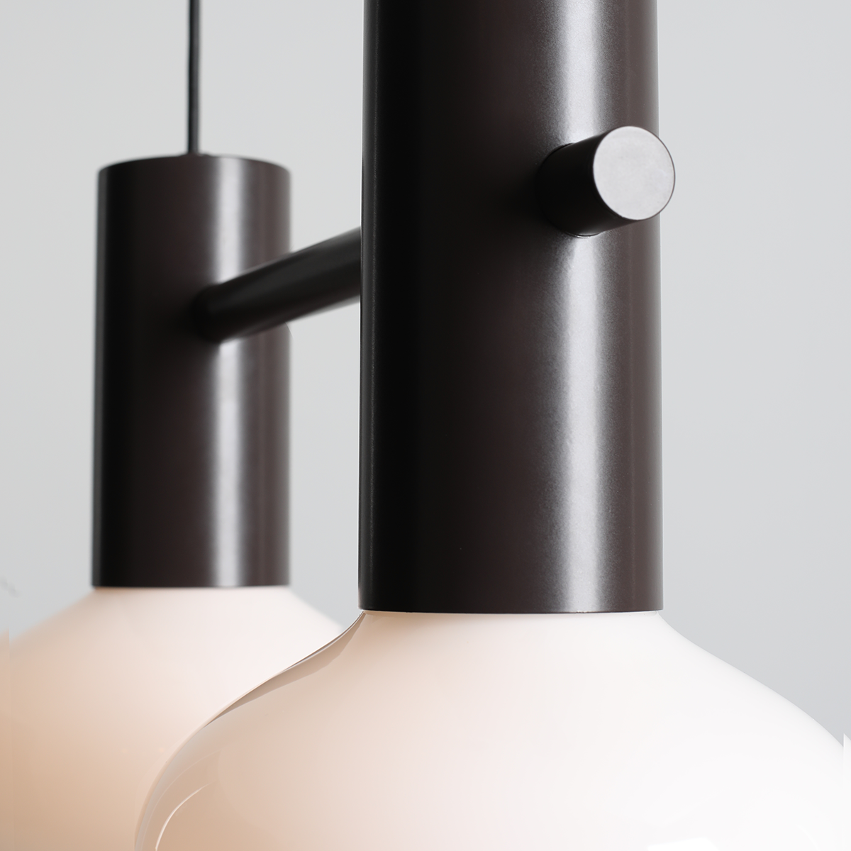 Lampa wisząca Flo Mokka z dwoma kloszami E14, w kolorze czarnym matowym. Klosze mają okrągły kształt, wykonane z białego szkła. Produkt zawieszony na cienkim, czarnym kablu, z widocznym elementem mocującym. Tło w jasnoszarym kolorze.