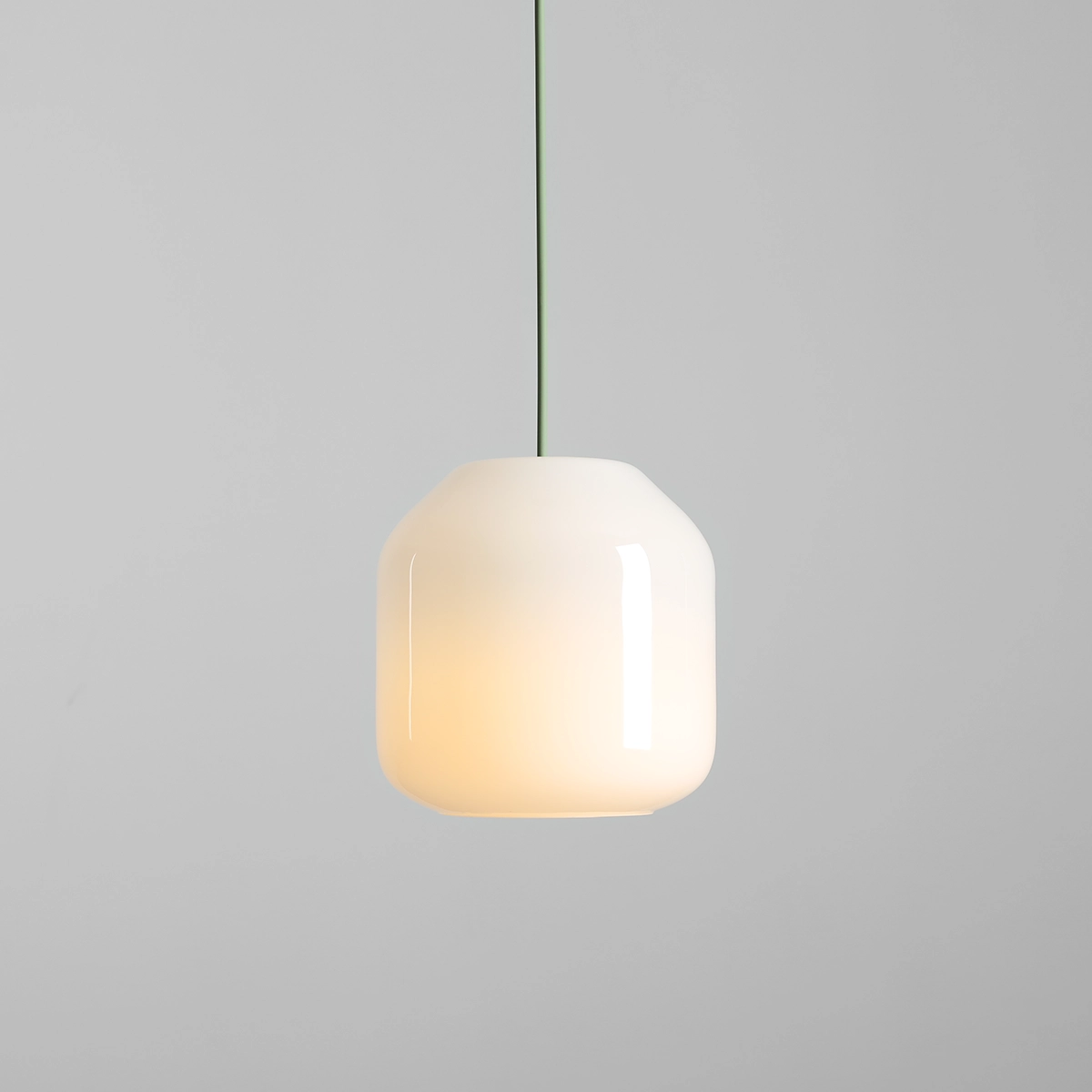 Lampa wisząca Flask Sage D18 z kloszem w kształcie sześcianu, wykonana z białego szkła, zawieszona na zielonym przewodzie. Emituje ciepłe światło, idealna do nowoczesnych wnętrz. Tło szare, minimalistyczne.