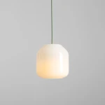 Lampa wisząca Flask Sage D18 z kloszem w kształcie sześcianu, wykonana z białego szkła, zawieszona na zielonym przewodzie. Emituje ciepłe światło, idealna do nowoczesnych wnętrz. Tło szare, minimalistyczne.