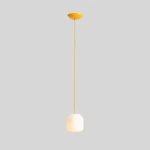 Lampa wisząca Flask Mimosa D18 w kolorze żółtym, z jednym gniazdem E14. Stojący klosz w kształcie lekko zaokrąglonego sześcianu, zawieszony na długim, żółtym przewodzie. Proste tło szare.