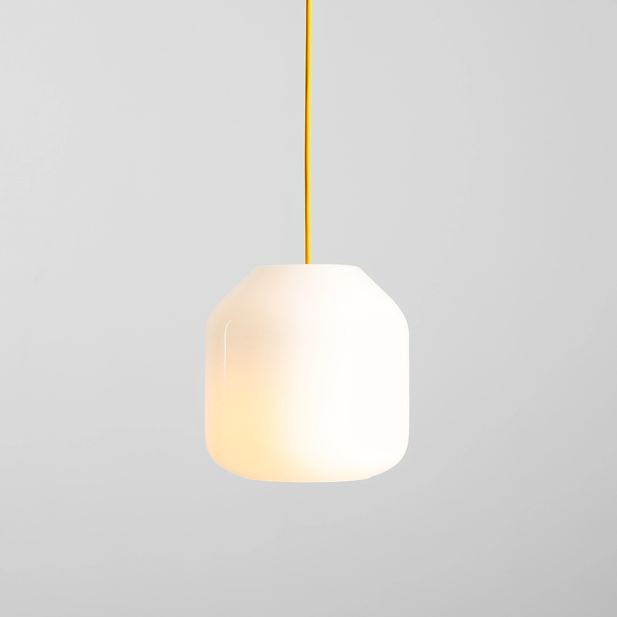 Lampa wisząca Flask Mimosa D18 z białym kloszem w kształcie stożka, zawieszona na żółtym przewodzie. Klosz wykonany z matowego materiału, emituje ciepłe światło. Ujęcie frontalne, na jednolitym szarym tle.