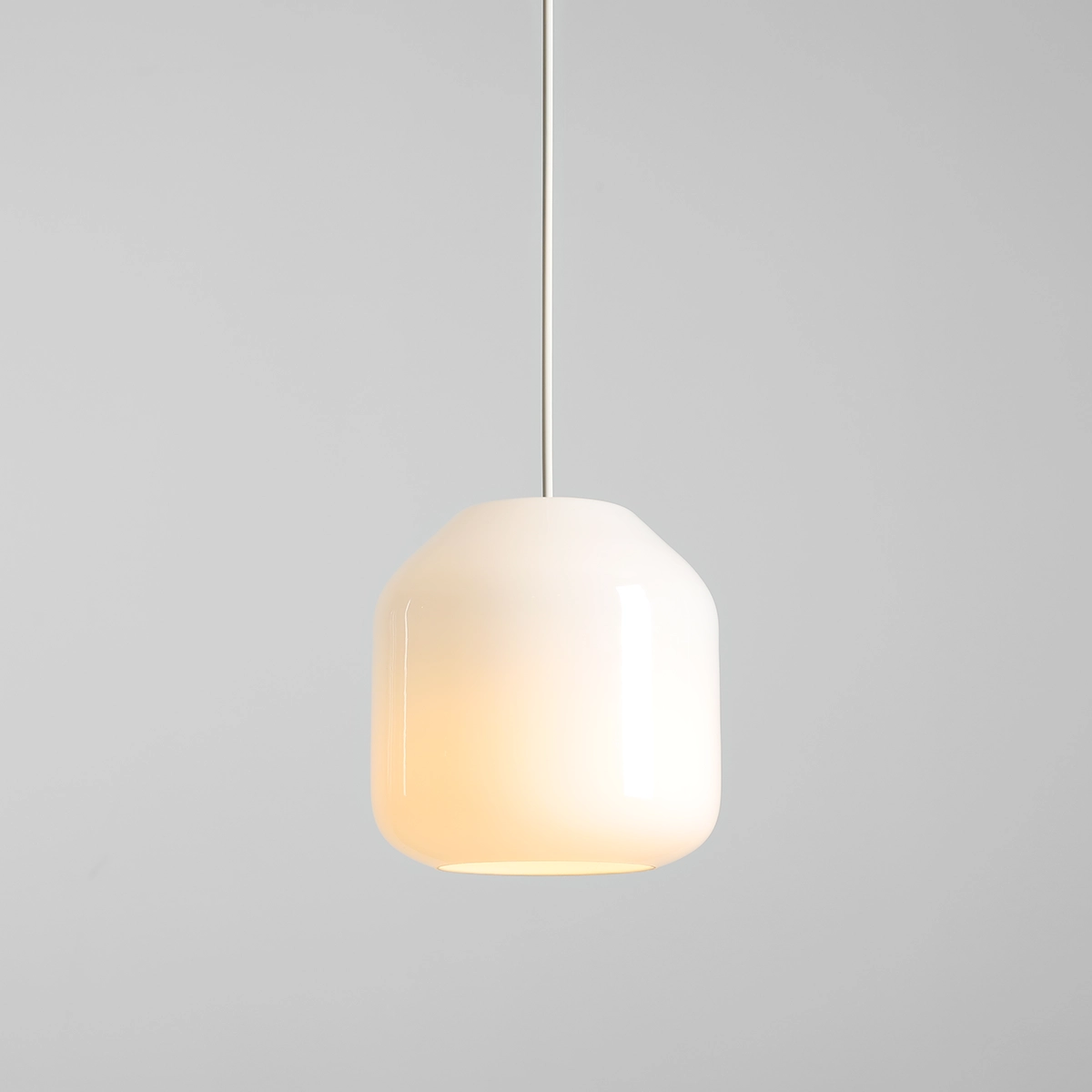 Kremowa lampa wisząca Flask Cotton D18 z jedną oprawą E14, o zaokrąglonym kształcie. Wisi na cienkim, białym przewodzie, emitując ciepłe światło. Tło w odcieniu szarości, co podkreśla minimalistyczny design.
