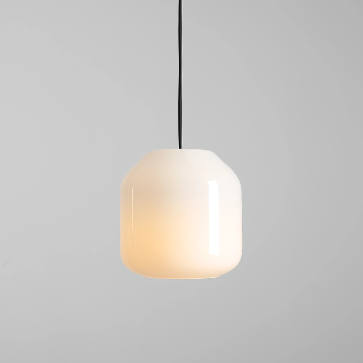 Lampa wisząca Flask Orchid D18 z kloszem w kształcie szklanej, matowej bryły w kolorze białym, zawieszona na czarnym przewodzie. Klosz emituje ciepłe światło, nadając elegancki charakter wnętrzu. Tło proste, szare.