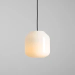 Lampa wisząca Flask Orchid D18 z kloszem w kształcie szklanej, matowej bryły w kolorze białym, zawieszona na czarnym przewodzie. Klosz emituje ciepłe światło, nadając elegancki charakter wnętrzu. Tło proste, szare.