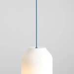 Lampa wisząca Flask Sapphire D19 z kloszem w kształcie butelki, wykonanym z białego szkła, zawieszona na niebieskim przewodzie. Klosz ma delikatne zaokrąglenia u góry, a źródło światła E27 jest widoczne w dolnej części. Tło jasnoszare.