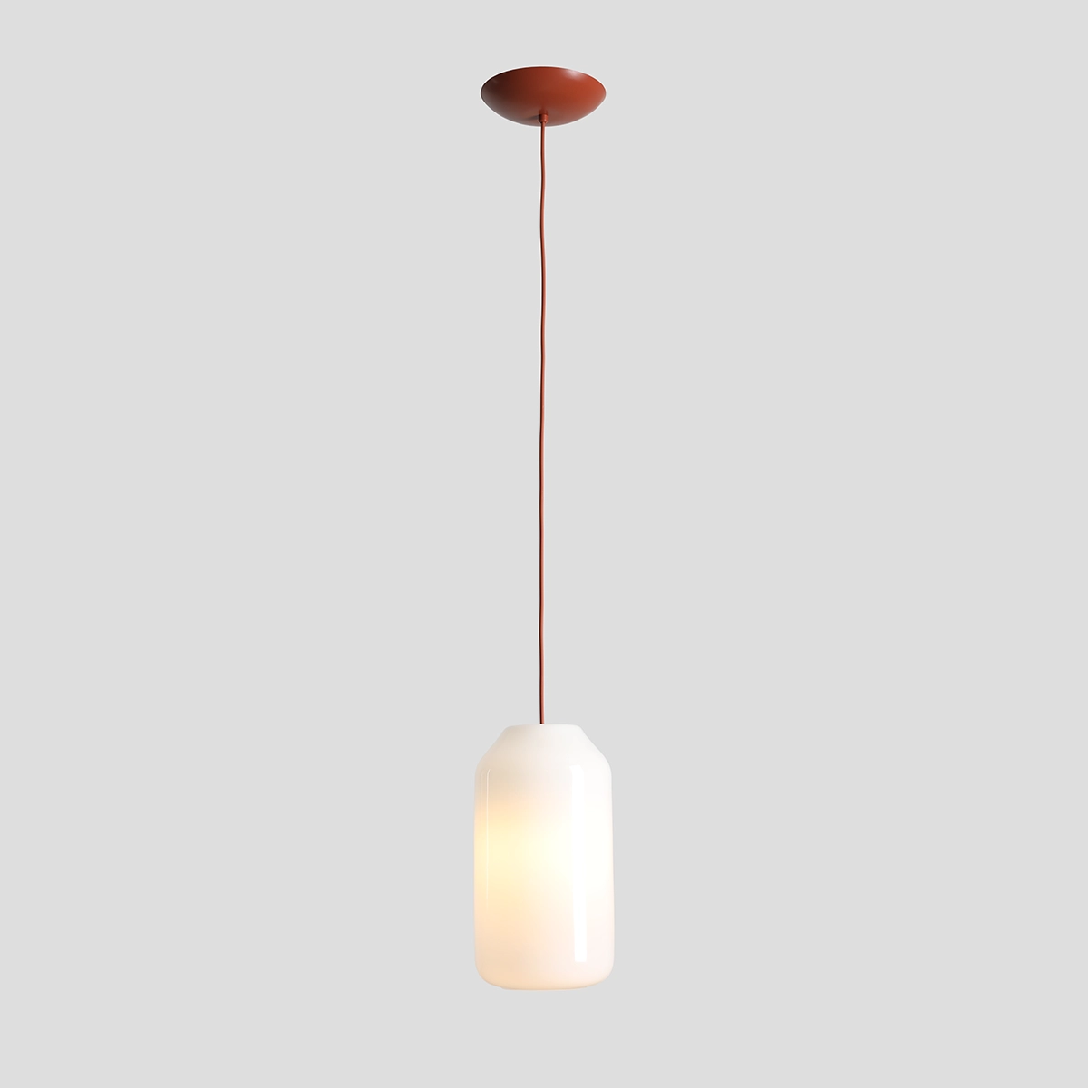 Lampa wisząca Flask Terra D19 z jednym gniazdem E27. Posiada cylindryczny klosz z matowego szkła w kolorze białym oraz ceglane detale. Zawieszona na cienkim, prostym przewodzie, montowana do sufitu. Tło w odcieniu szaro-beżowym.