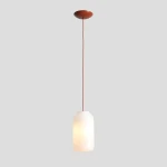 Lampa wisząca Flask Terra D19 z jednym gniazdem E27. Posiada cylindryczny klosz z matowego szkła w kolorze białym oraz ceglane detale. Zawieszona na cienkim, prostym przewodzie, montowana do sufitu. Tło w odcieniu szaro-beżowym.