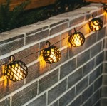 Girlanda ogrodowa solarna Glovi z 20 LED w czarnych, siatkowych kloszach, zawieszona na murze. Długość 4 m, emitująca ciepłe światło, idealna do dekoracji przestrzeni na zewnątrz.