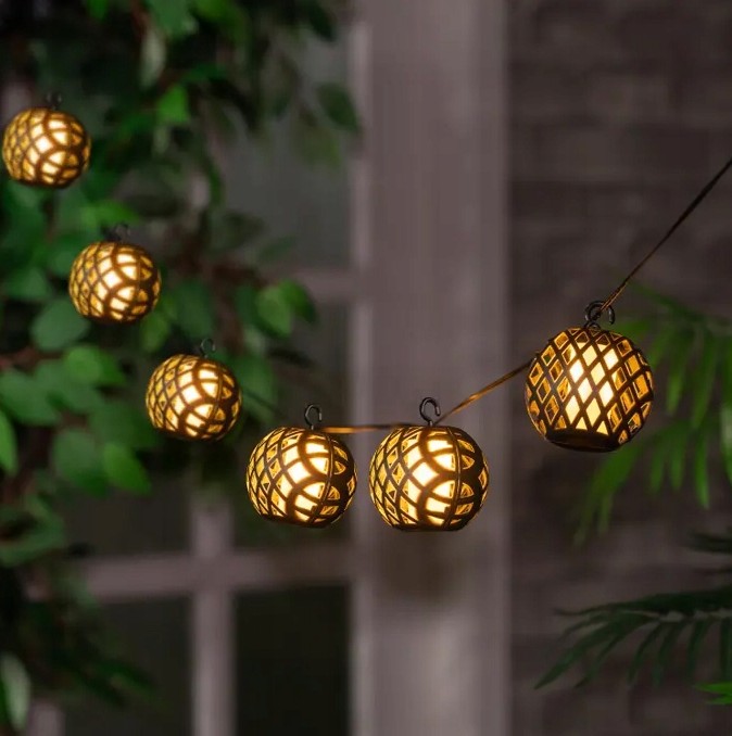 Girlanda ogrodowa solarna Glovi z 20 LED w czarnych, siatkowych kulach. Długość 4 m, zawieszona w otoczeniu zieleni, emitująca ciepłe, żółte światło. Kule mają dekoracyjne wzory, idealne do oświetlenia przestrzeni na zewnątrz.
