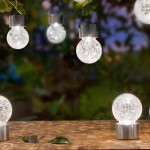 Lampka wisząca solarna Glovi 6000K, zimna biała, z przezroczystą kulą z efektem crackle. Produkt zawieszony na metalowych uchwytach, umieszczony w ogrodzie, z widocznymi detalami oświetlenia w tle.