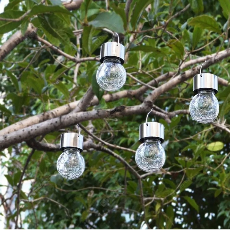 Lampka wisząca solarna Glovi 6000K w kolorze zimnej białej, z przezroczystym, teksturowanym kloszem i metalowym uchwytem. Cztery lampki zawieszone na gałęziach drzewa, w otoczeniu zieleni. Klosze mają okrągły kształt.
