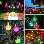 Lampka wisząca solarna RGB w różnych kolorach (zielony, czerwony, niebieski, żółty, różowy) umieszczona w aranżacjach ogrodowych, w tym zewnętrznych, na gałęziach drzew oraz nad stołem. Szklane kulki z metalowym mocowaniem, emitujące wielobarwne światło.