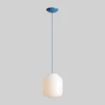 Lampa wisząca Flask Sapphire D27 z jednym gniazdem E27, w kolorze białym z niebieskim stelażem. Owalny klosz o gładkiej powierzchni, zawieszony na cienkim, niebieskim przewodzie, umieszczony na jasnoszarym tle.