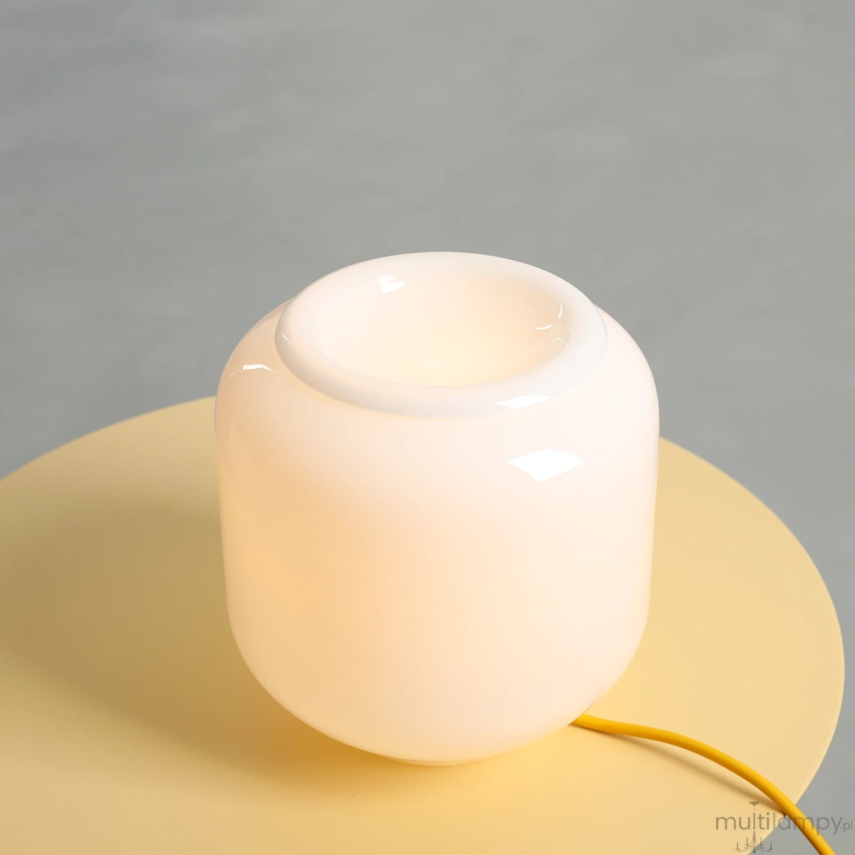 Lampa stołowa Flask Mimosa w kolorze białym z żółtym kablem, o zaokrąglonym, szklanym kształcie. Ujęcie z góry, widać otwór na żarówkę E14, lampa umieszczona na okrągłym, żółtym blacie.