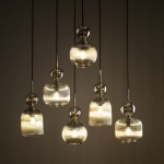 Lampa wisząca Sophia z sześcioma kloszami E14 w kolorze bursztynowym. Klosze mają różne kształty, są szklane z żłobieniami, zawieszone na czarnych linkach. Błyszczące detale metalowe podkreślają elegancję lampy. Tło w odcieniu ciemnym.