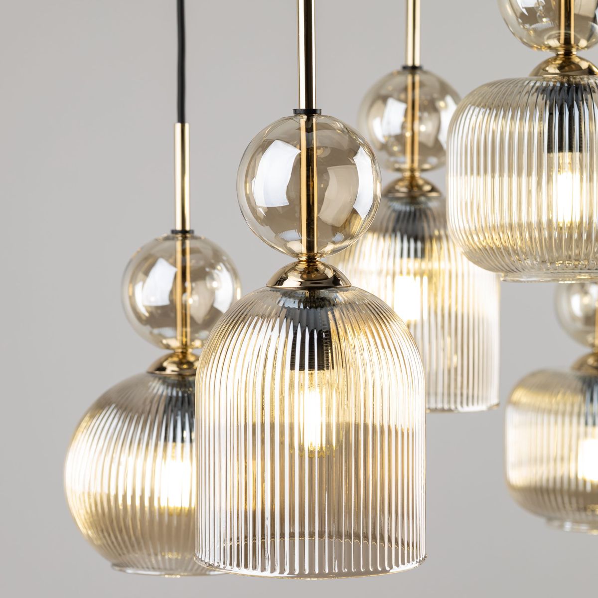 Lampa wisząca Sophia z sześcioma kloszami E14 w kolorze bursztynowym. Klosze mają żłobioną fakturę i zaokrąglony kształt, z przezroczystymi elementami. Zawieszona na cienkich, złotych linkach, tworzy elegancki efekt w nowoczesnym wnętrzu.