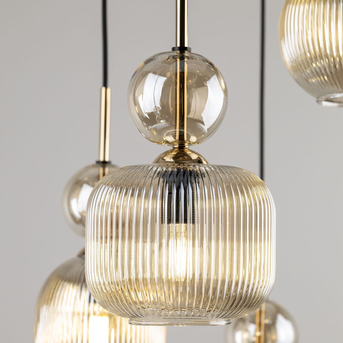 Lampa wisząca Sophia z sześcioma oprawami E14, wykonana z bursztynowego, żebrowanego szkła. Zawiera okrągłe, przezroczyste elementy i złote detale. Wisi na czarnym kablu, tworząc elegancki akcent w aranżacji wnętrza.