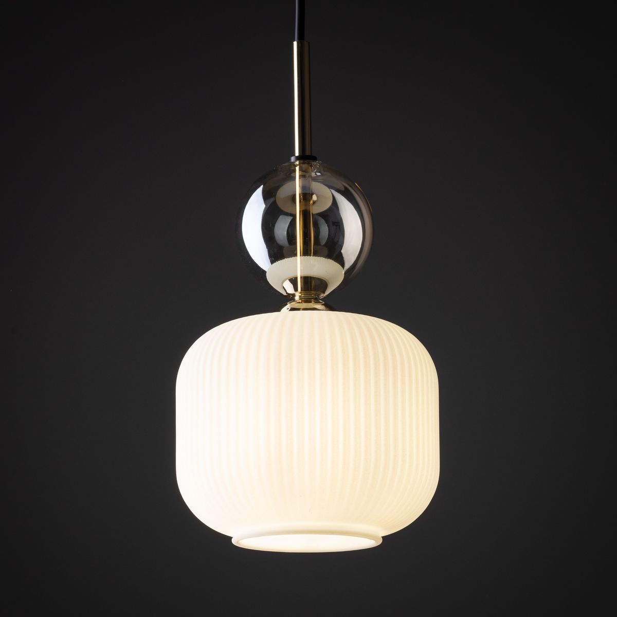 Lampa wisząca Sophia z kloszem w kolorze białym, o zaokrąglonym kształcie z pionowymi żłobieniami. Górna część z przezroczystego szkła oraz metalowym wykończeniem w odcieniu złotym. Zawieszona na czarnym przewodzie, idealna do nowoczesnych wnętrz.