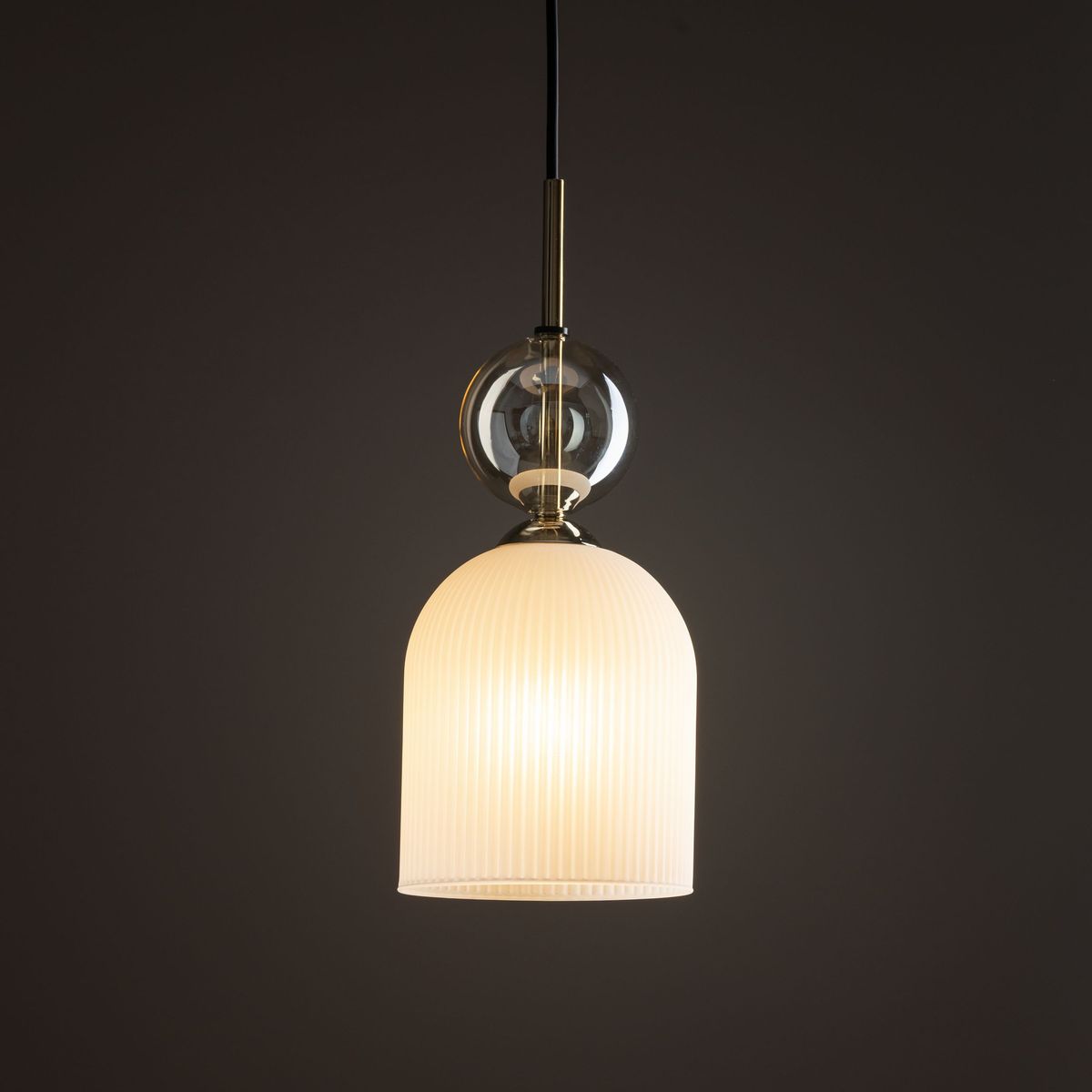Lampa wisząca Sophia 1xE14 w białym kolorze z plisowanym kloszem, u góry z przezroczystą kulą. Zawieszona na czarnym przewodzie, z metalowymi detalami w kolorze złotym. Idealna do nowoczesnych wnętrz.