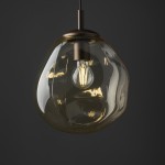 Lava Brown D25 to brązowa lampa wisząca z kloszem w kształcie kropli, wykonana z przezroczystego szkła. W centralnej części znajduje się żarówka E27. Lampa zawieszona na stylowym, metalowym mocowaniu w ciemnym kolorze, na tle szarym.