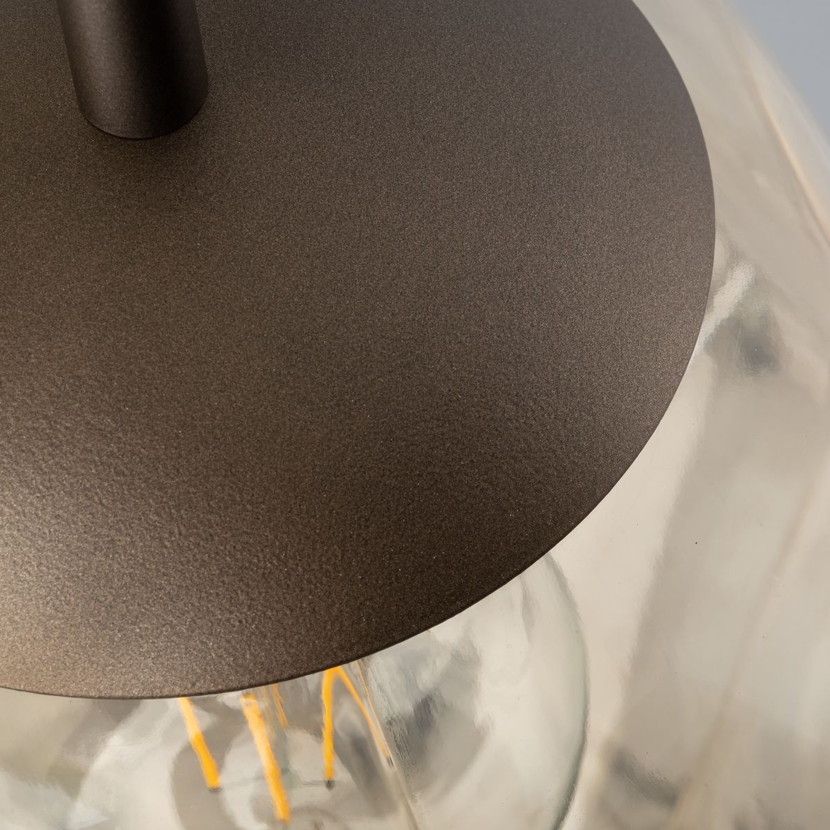 Lampa wisząca Lava Brown D35 z brązowym, matowym wykończeniem. Widoczny metalowy element mocujący oraz przezroczysta klosz, ukazujący żarówkę E27. Ujęcie z góry, akcentujące detale i teksturę materiału.