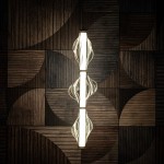 Lampa wisząca LED Elva 22W z mosiężnymi detalami i bursztynowym kloszem, w kształcie fal, zawieszona w centralnej pozycji. Tło w odcieniach drewna z geometrycznym wzorem, podkreśla elegancki design lampy.