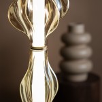 Lampa wisząca LED Elva 22W 3000K w kolorze mosiądzu z bursztynowym kloszem. Zbliżenie na elegancki, falisty kształt klosza oraz źródło światła, w tle widoczny ceramiczny wazon w neutralnych odcieniach.