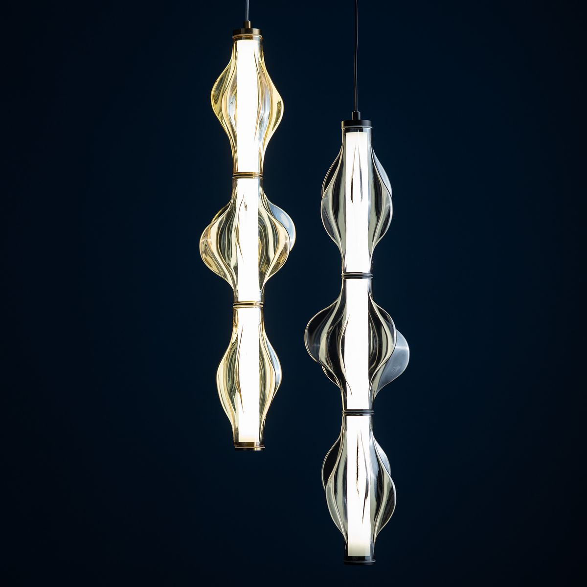 Lampa wisząca LED Elva 22W, 3000K, w kolorze mosiądzu i bursztynu. Dwie szklane formy o falistej strukturze, zawieszone na cienkich kabelkach, emitujące ciepłe światło, na ciemnym tle.