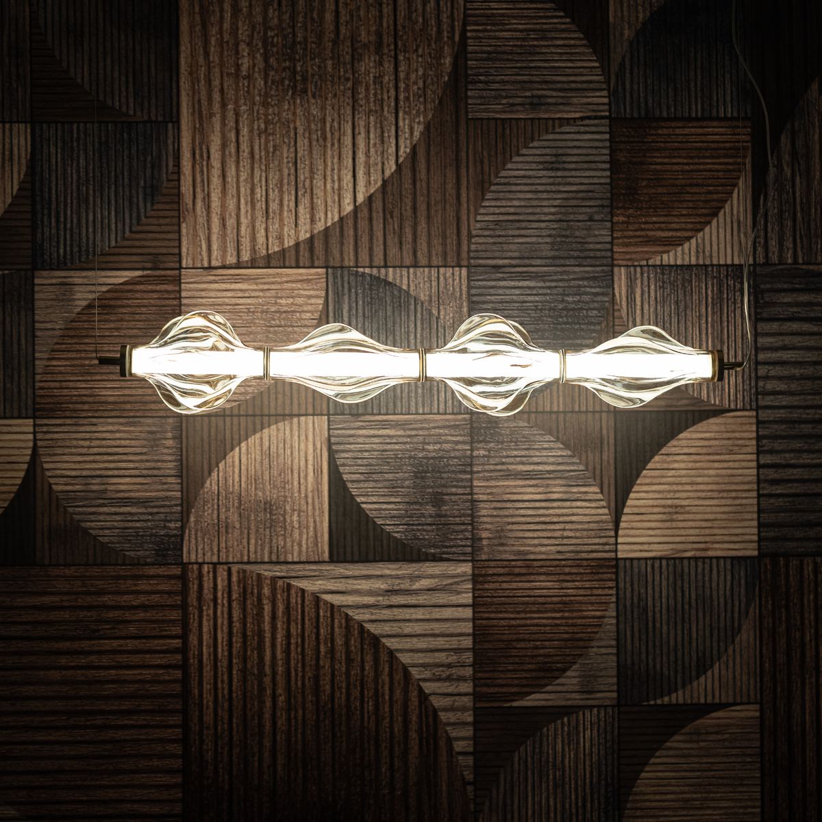 Lampa wisząca LED Elva 30W, ciepła barwa 3000K, mosiężna konstrukcja z bursztynowymi kloszami. Ujęcie z góry, zamontowana na tle drewnianych paneli o różnych fakturach. Klosze mają falisty kształt, rozpraszając światło.
