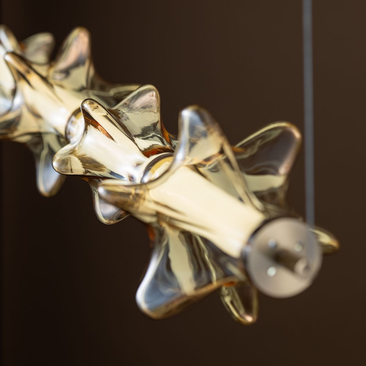 Lampa wisząca LED Elva 30W w kolorze mosiądzu z bursztynowymi kloszami, o dekoracyjnym kształcie gwiazdy. Widok zbliżony, ukazujący detale kloszy oraz metalową podstawę mocującą.