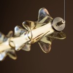Lampa wisząca LED Elva 30W z bursztynowym kloszem w kształcie gwiazd, z metalowym mocowaniem w kolorze mosiądzu. Zbliżenie na detal klosza z widocznym światłem LED, zawieszona na cienkim przewodzie. Tło w ciemnym odcieniu.