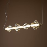 Lampa wisząca LED Elva 30W, 3000K, w kolorze mosiądzu i bursztynu. Wyposażona w szklane klosze o falistym kształcie, zawieszona na cienkim przewodzie, z widocznym źródłem światła w centralnej części. Tło w stonowanym odcieniu.