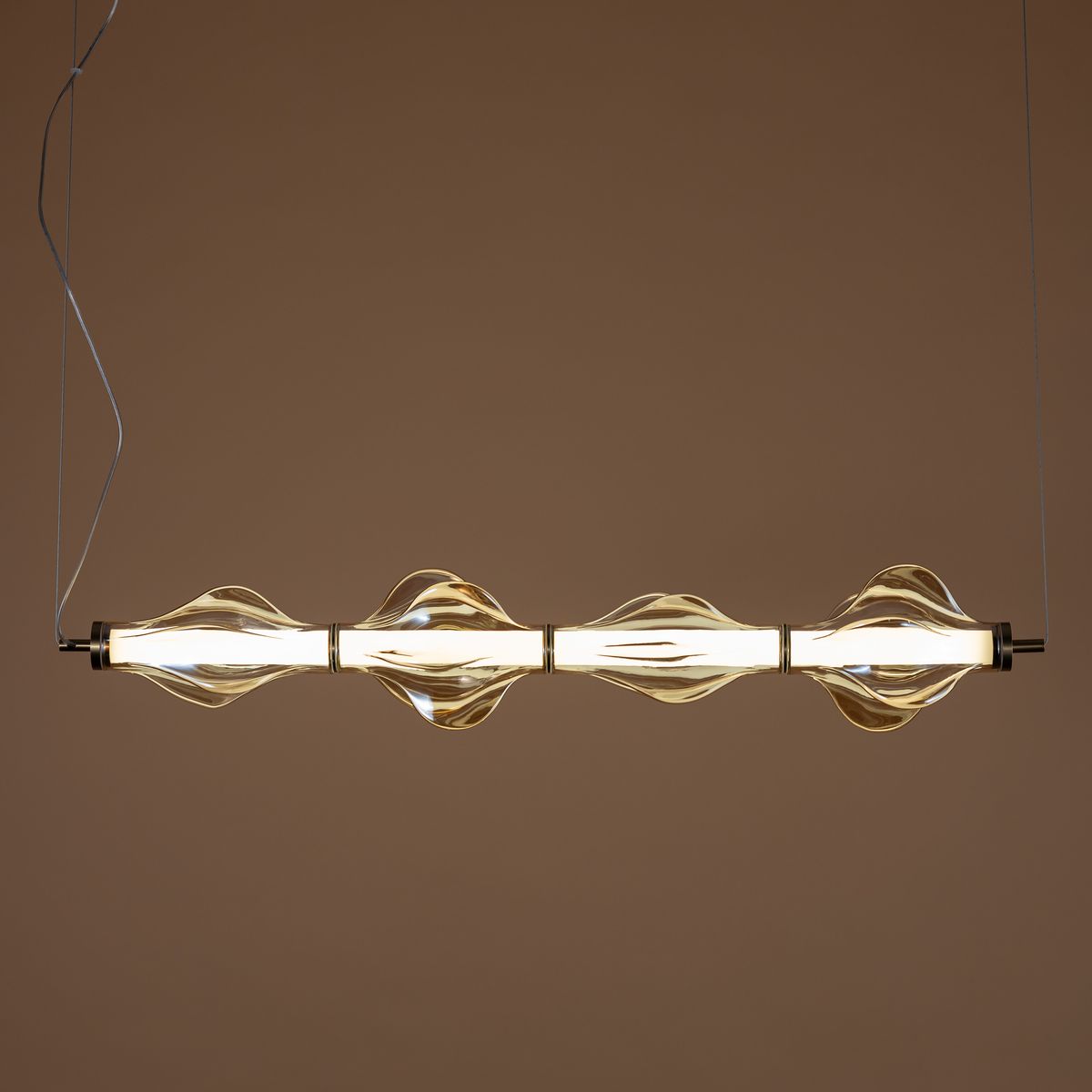 Lampa wisząca LED Elva 30W w kolorze mosiądzu i bursztynu, z pięcioma szklanymi kloszami w kształcie fal, zawieszona na cienkim przewodzie, emitująca ciepłe światło o temperaturze 3000K, na jednolitym tle.