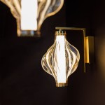 Kinkiet LED Elva o mocy 8W i barwie 3000K, z mosiężnym uchwytem. Szklany klosz w bursztynowym odcieniu, o falistym kształcie, montowany na ścianie, z wyraźnym źródłem światła w centralnej części.