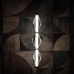 Lampa wisząca LED Elva 22W 3000K w kolorze czarnym/grafitowym, z trzech przeszklonych elementów o falistym kształcie. Zawieszona na minimalistycznym stelażu, w otoczeniu drewnianej, geometrycznej ściany.