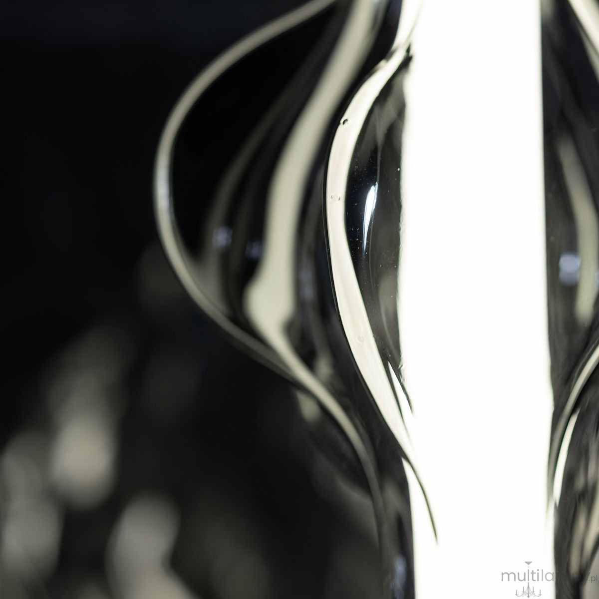 Lampa wisząca LED Elva 22W w kolorze czarnym/grafitowym, o smukłej, falistej formie. Zbliżenie na detal obudowy z lustrzanym wykończeniem, odbijającym światło. W tle ciemne, jednolite tło, podkreślające elegancję lampy.