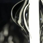 Lampa wisząca LED Elva 22W w kolorze czarnym/grafitowym, o smukłej, falistej formie. Zbliżenie na detal obudowy z lustrzanym wykończeniem, odbijającym światło. W tle ciemne, jednolite tło, podkreślające elegancję lampy.