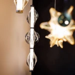 Elva lampa wisząca LED 22W 3000K w kolorze czarnym i grafitowym, z charakterystycznym, przezroczystym kloszem o falistym kształcie, zawieszona w pionie. Tło ciemne, widać także inne lampy w blurze.