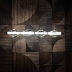 Lampa wisząca LED Elva 30W w kolorze czarnym i grafitowym. Posiada cztery przezroczyste klosze o falistym kształcie, zawieszona poziomo na czarnym przewodzie. Tło stanowi wzorzysty, drewniany panel. Temperaturę barwową światła wynosi 3000K.