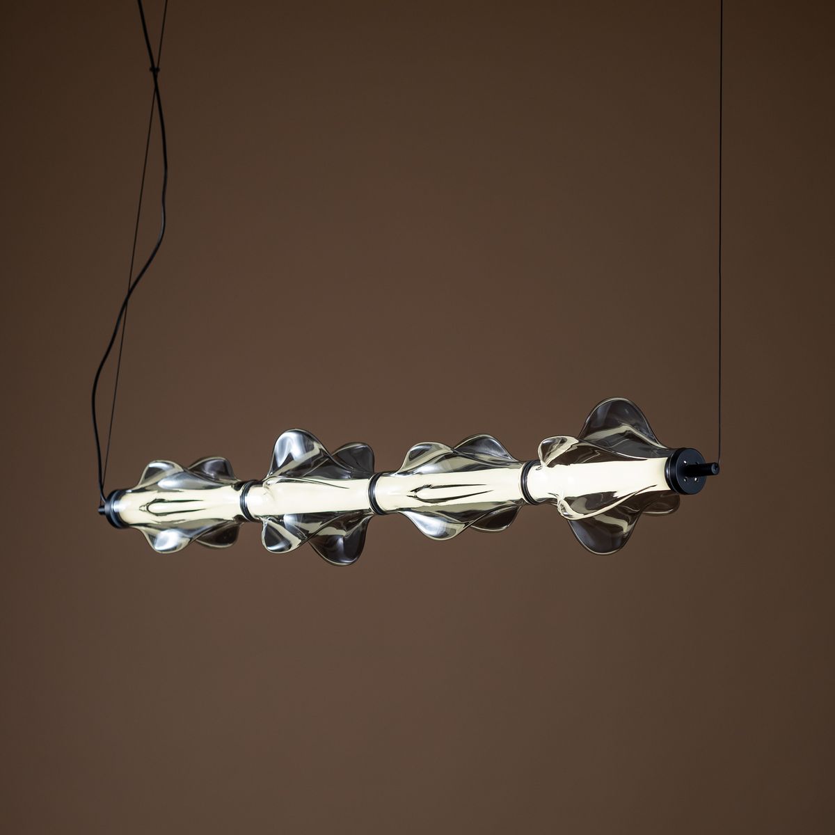 Lampa wisząca LED Elva 30W 3000K w kolorze czarnym i grafitowym, z przezroczystym, falistym kloszem. Ujęcie frontalne, zawieszona na cienkim przewodzie, z widocznymi detalami kształtu klosza i źródła światła. Tło w odcieniu brązowym.