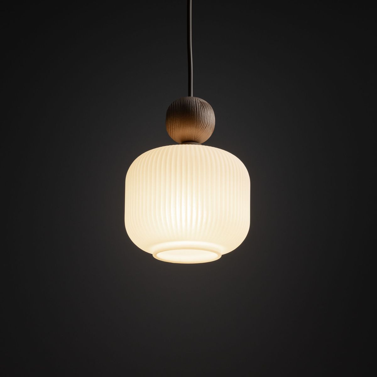 Lampa wisząca Ballo w odcieniu beżowym z kloszem w kształcie półkuli, z widoczną teksturą żłobień. U góry umieszczona drewniana kula. Zawieszona na cienkim przewodzie, na ciemnym tle. Przeznaczona do jednego źródła światła E14.