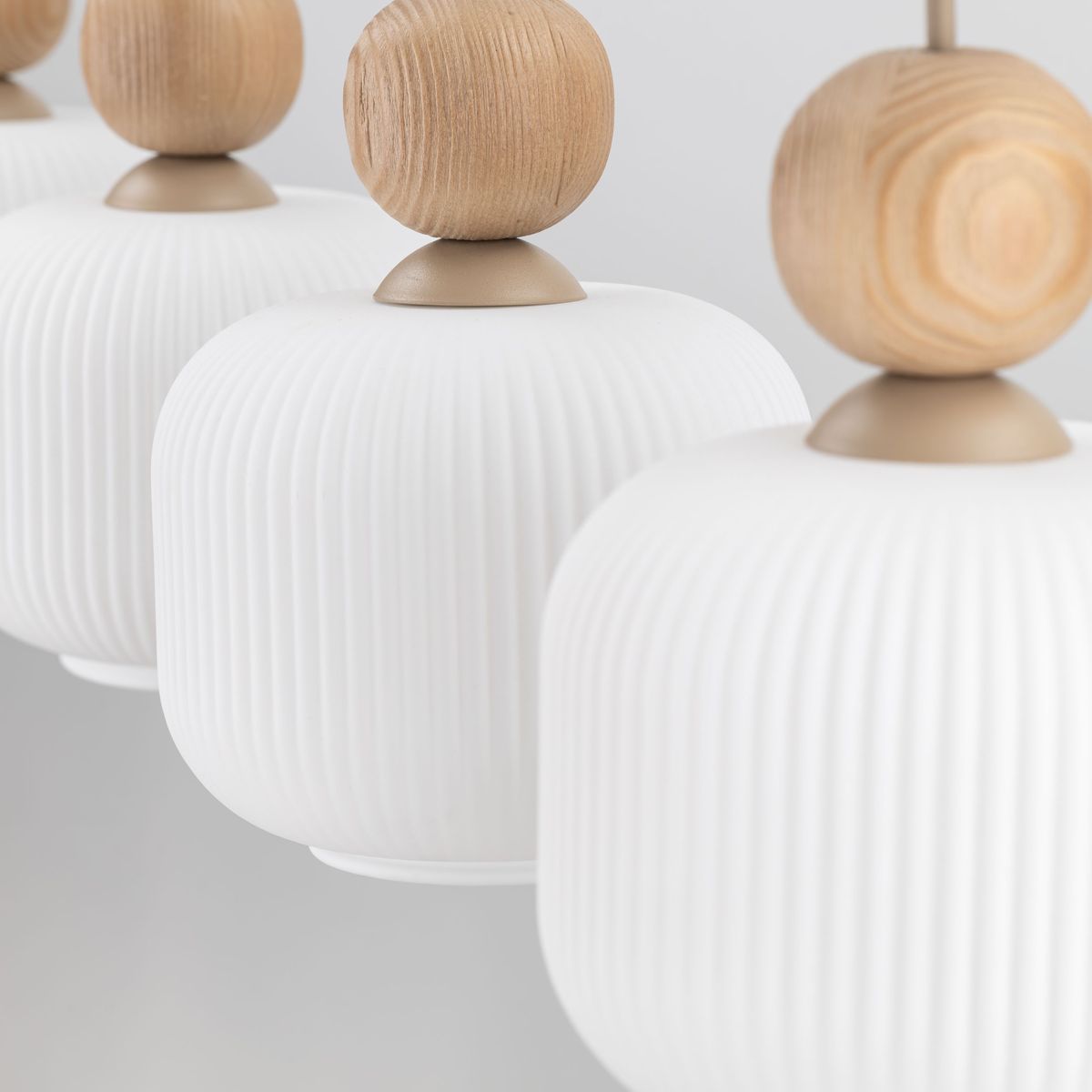 Lampa wisząca Ballo w beżowym kolorze z czterema szklanymi kloszami o teksturowanej powierzchni i drewnianymi elementami. Produkt zawieszony, widoczny z bliska, z eleganckim detalem w postaci kulistych uchwytów.