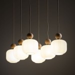 Ballo lampa wisząca z sześcioma kloszami E14 w kolorze beżowym. Klosze mają delikatne rowki, a u góry znajdują się drewniane kulki. Lampa zawieszona na cienkich, białych przewodach, prezentuje się nowocześnie na ciemnym tle.