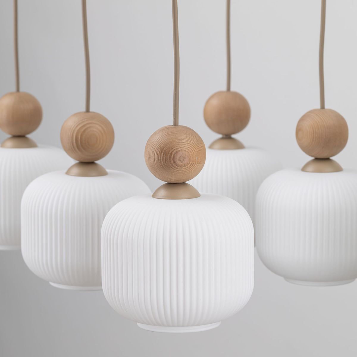 Ballo lampa wisząca w beżowym kolorze, składająca się z sześciu kloszy z białego, teksturowanego szkła, z dekoracyjnymi drewnianymi kulkami u góry. Klosze mają owalny kształt, zawieszone na cienkich linkach, w prostym, eleganckim stylu.