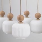 Ballo lampa wisząca w beżowym kolorze, składająca się z sześciu kloszy z białego, teksturowanego szkła, z dekoracyjnymi drewnianymi kulkami u góry. Klosze mają owalny kształt, zawieszone na cienkich linkach, w prostym, eleganckim stylu.