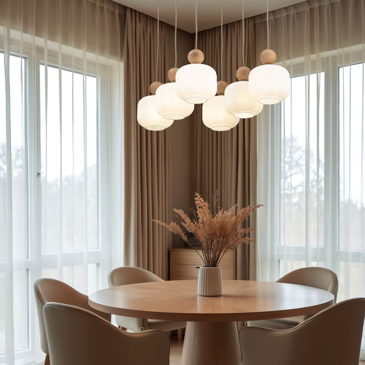 Lampa wisząca Ballo w kolorze beżowym, z sześcioma kloszami E14, zawieszona nad okrągłym drewnianym stołem. Klosze mają zaokrąglony kształt z żłobioną fakturą i drewnianymi elementami. W tle zasłony i bukiet suszonych kwiatów.