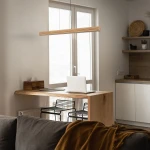 Lampa wisząca LED Viga Wood 14W 3000K w kolorze czarnym i sosnowym, w prostokątnym kształcie, zawieszona nad drewnianym blatem biurka. Tło jasne, z oknem i minimalistycznym wystrojem wnętrza.